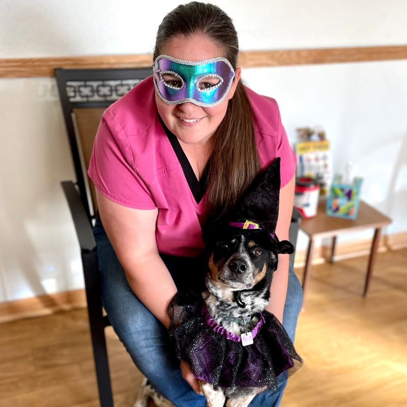 a person wearing a mask and sitting on a chair with a dog
